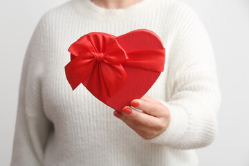 Woman with red manicure holding heart shaped gift box on white background. Valentine's Day celebration