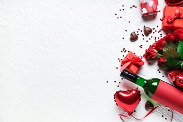 Bottle of wine with gift boxes, chocolate candies, red roses and heart shaped air balloons on white...