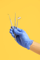 Male dentist hand with dental tools on yellow background