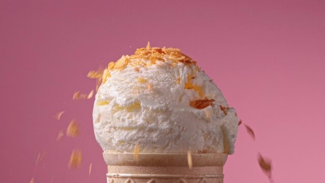 close-up of decorative waffle crisps falling on an ice cream ball on a pink background, slow motion video