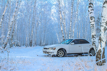 white car in a winter forest on a snowy clearing at sunset