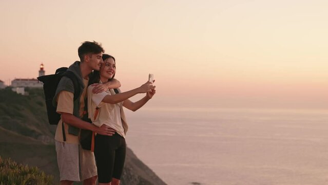 A young couple embraces, capturing the magic of a breathtaking sunset on the ocean after a day of hiking
