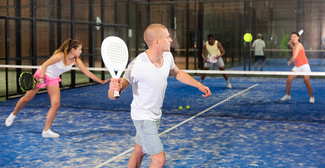 Portrait of concentrated paddle tennis player preparing to hit forehand to return ball on indoor...