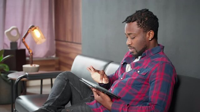 carefree african american man resting at home and surfing internet by tablet, guy shopping online
