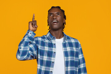 Black man in plaid shirt pointing upwards, looking inspired against yellow background