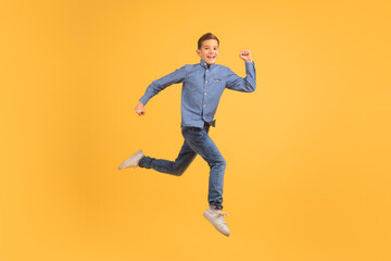 Fototapeta na wymiar Dynamic teen boy jumping in air against yellow studio background