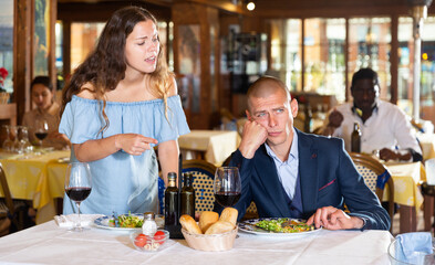 Fototapeta na wymiar Annoyed woman arguing with boyfriend in restaurant sitting at served table