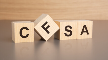 four wooden cubes with the letters CFSA on the bright surface of a brown table, business concept