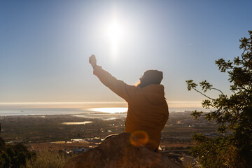 A hiker captures a selfie while sitting at the summit of a mountain, greeting the daybreak over a...