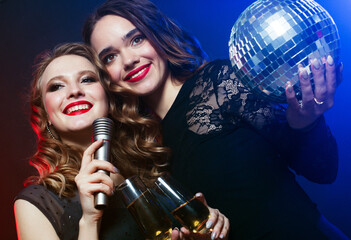 two beautiful stylish girls singing karaoke at the club - obrazy, fototapety, plakaty