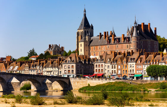 Scenic summer view of Gien townscape overlooking arched bridge across Loire river and medieval Chateau de Gien dominating over residential houses on sunny day, France