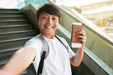 Cheerful asian man taking selfie, showing passport and tickets