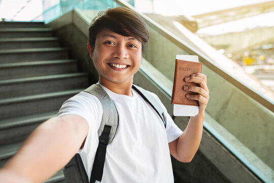 Cheerful asian man taking selfie, showing passport and tickets