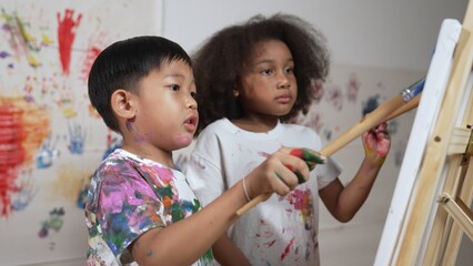 Happy creative african girl painted or draw canvas together with asian boy. Group of playful...