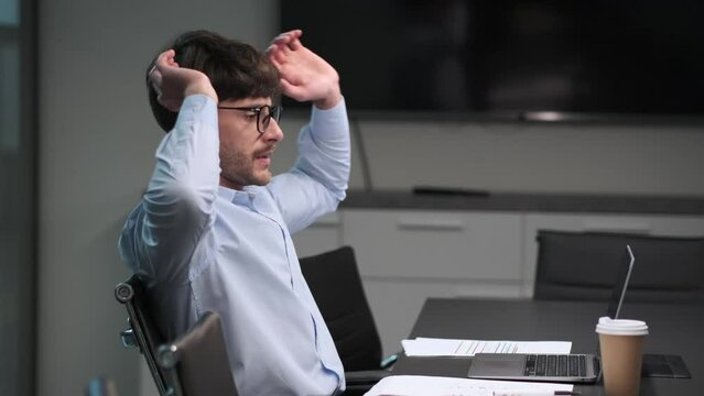Tired businessman takes a moment to stretch at desk. His fatigued muscles find relief in the simple act, a brief pause in schedule, reflecting resilience and determination.
