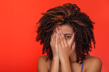 Afro-American woman hiding behind her hands, making a fearful expression