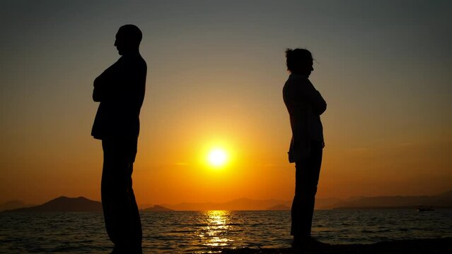 Quarreled couple silhouettes on beach. A view of quarreled couple silhouette stand on the shore against orange sky in the evening time.