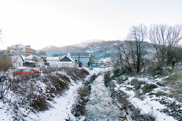 Mountain river flows between the snow-covered banks of a village at the foot of the mountains