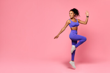 African sporty woman in activewear jumps performing cardio workout, studio