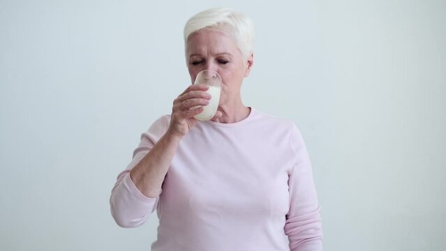 Senior Caucasian woman delicately takes a sip of milk from a glass, gesture reflecting both grace and vitality. Lips touch the rim of the glass with elegance, and eyes convey a sense of satisfaction.