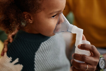 Close up shot with high angle of African American girl child inhaling medicine with nebulizer mask on face - obrazy, fototapety, plakaty