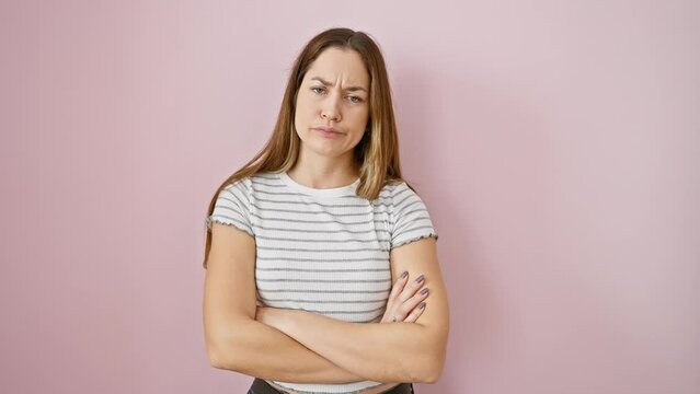 Skeptical, nervous young woman with crossed arms and disapproving expression. blue-eyed beauty standing against pink isolated background. negative vibes overflow.