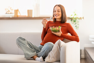 Smiling Pregnant Woman Sitting On Couch, Enjoying Fresh Vegetables Indoor