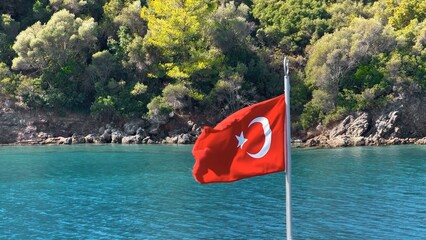 Turkish flag waving on the bow of the yacht on a boat tour. Gokova Bay which is mentioned in...