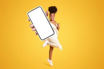 Excited cheerful young african american lady in dress showing phone - obrazy, fototapety, plakaty