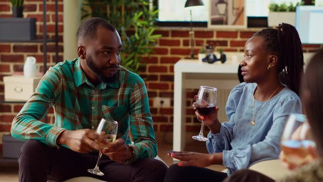 African american man at apartment party talking with woman sharing interesting story, flirting with her. Guest at home gathering interested in charming BIPOC host, chatting with her