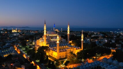 Obraz premium Süleymaniye Mosque built by Architect Sinan in 16th century in Istanbul, Turkey. Drone flies towards illuminated Suleymaniye Mosque on a Ramadan early morning. Aerial view 
