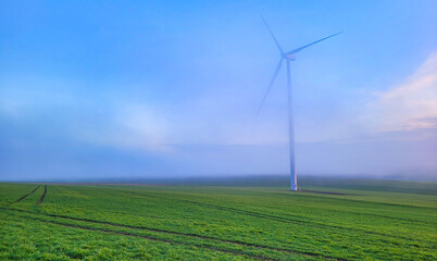 Turbina wiatrowa w mgłach o poranku na zielonych polach.