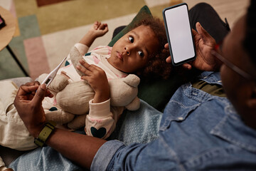 Top down view of unwell African American little girl on bed while her unrecognizable father holding...