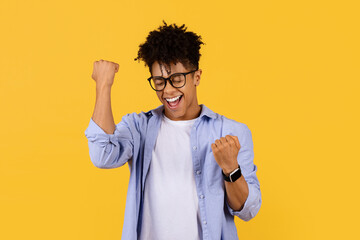 Exuberant black male student celebrates success on yellow background