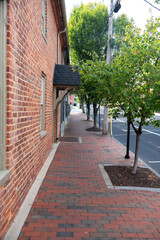 Fototapeta na wymiar Brick sidewalk along the walls of brick houses. Trees along the road