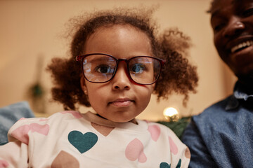 Medium close up shot of African American girl looking at camera wearing fathers big glasses and...