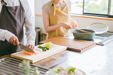 キッチンで料理をする夫婦・包丁で野菜を切る男性
 - obrazy, fototapety, plakaty