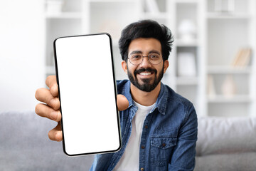 Friendly young indian man with glasses smiling while presenting blank smartphone screen