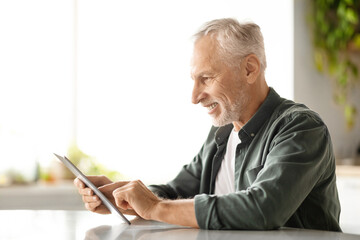 Delighted elderly man using digital tablet in kitchen