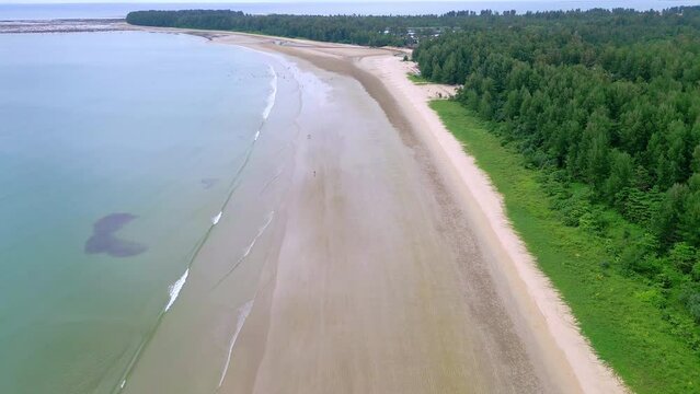 Descending aerial view of a large, quiet tropical sandy beach