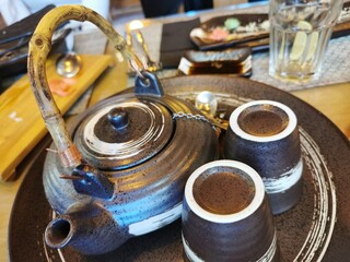 A close-up of an oriental-style brown cutlery set comprising a teapot, two glasses and a tea saucer. 