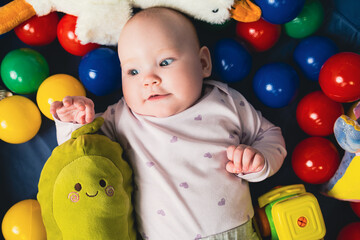 top view of cute infant baby girl lying on floor among colorful toys