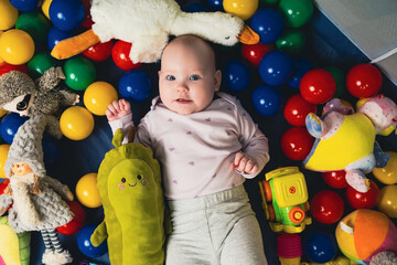 Fototapeta na wymiar top view of cute infant baby girl lying on floor among colorful toys