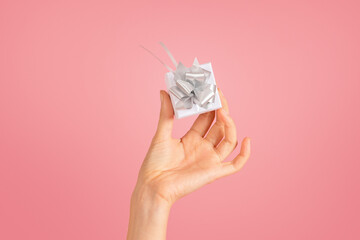 Delicate female hand holding a small, white gift with a shimmering silver bow