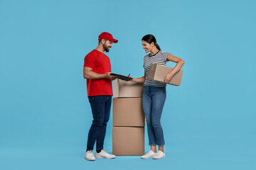 Smiling woman signing order receipt on light blue background. Courier delivery
