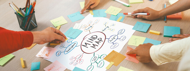 Professional startup group share creative marketing idea by using mind map. Young skilled business people brainstorm business plan while writing sticky notes. Focus on hand. Closeup. Variegated.