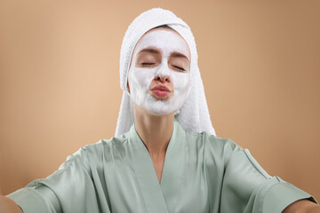 Woman with face mask taking selfie on beige background. Spa treatments