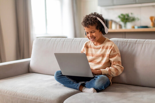 Little black boy wearing headphones using laptop computer at home