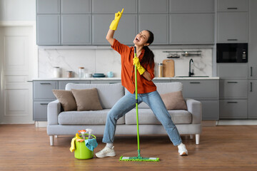 Joyful young woman dancing with mop in home interior - obrazy, fototapety, plakaty