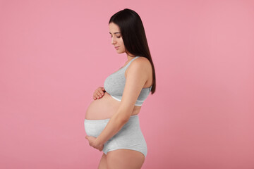Beautiful pregnant woman in comfortable maternity underwear on pink background